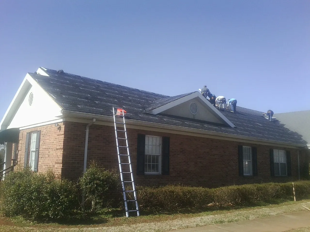 Crew tearing shingles off a brick ranch roof with a ladder set — Emergency Roof Repair work by our crew in Glen Dale