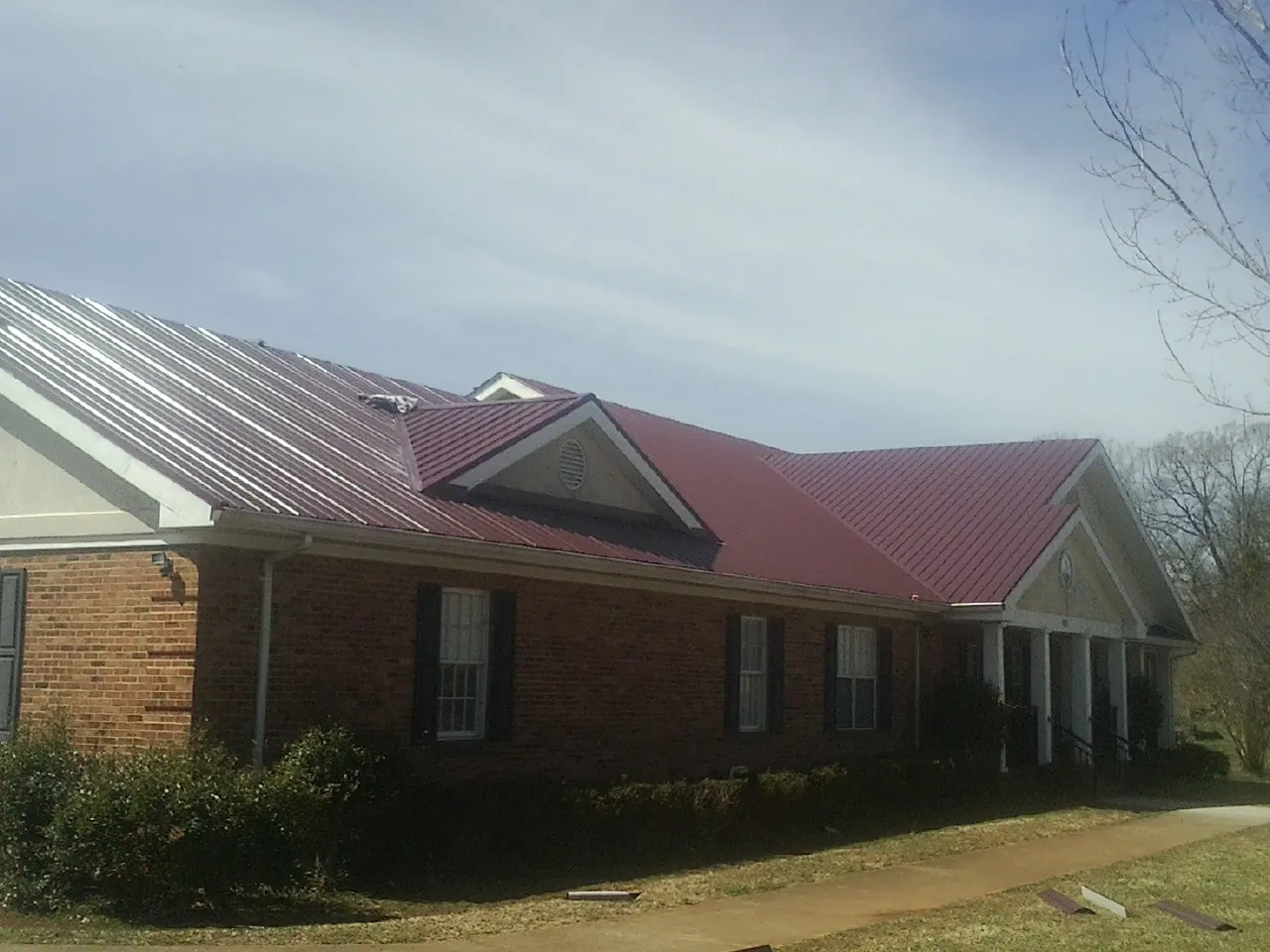 Red metal roof with gabled entries on a long brick building, from a Hail Damage Roof Repair job in Glen Dale