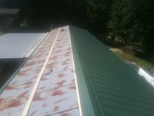 Old rusted panels beside newly installed green metal roofing — Wind Damage Roof Repair by Roofing Brothers in Glen Dale