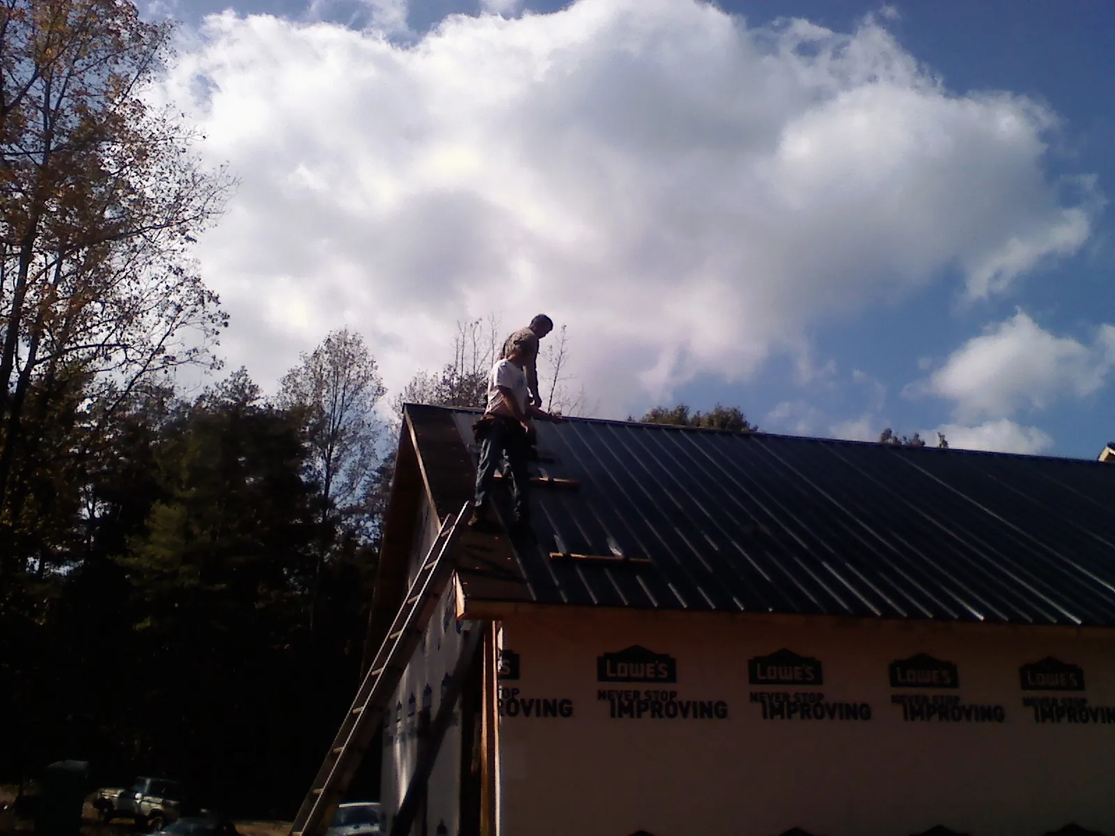 Roofer fastening dark metal panels high against a cloudy sky, from a Roof Inspection job in Glen Dale