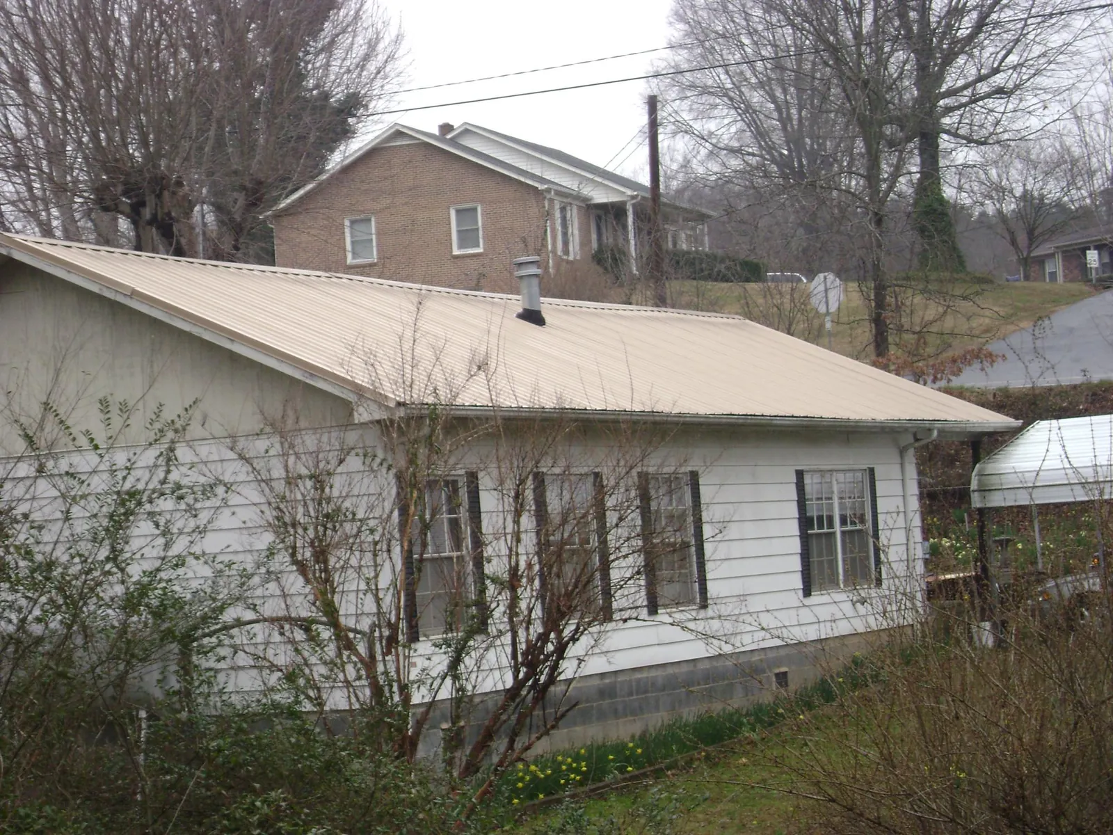 Tan metal roof on a white sided house set into a hillside — Commercial Roofing by Roofing Brothers in Glen Dale