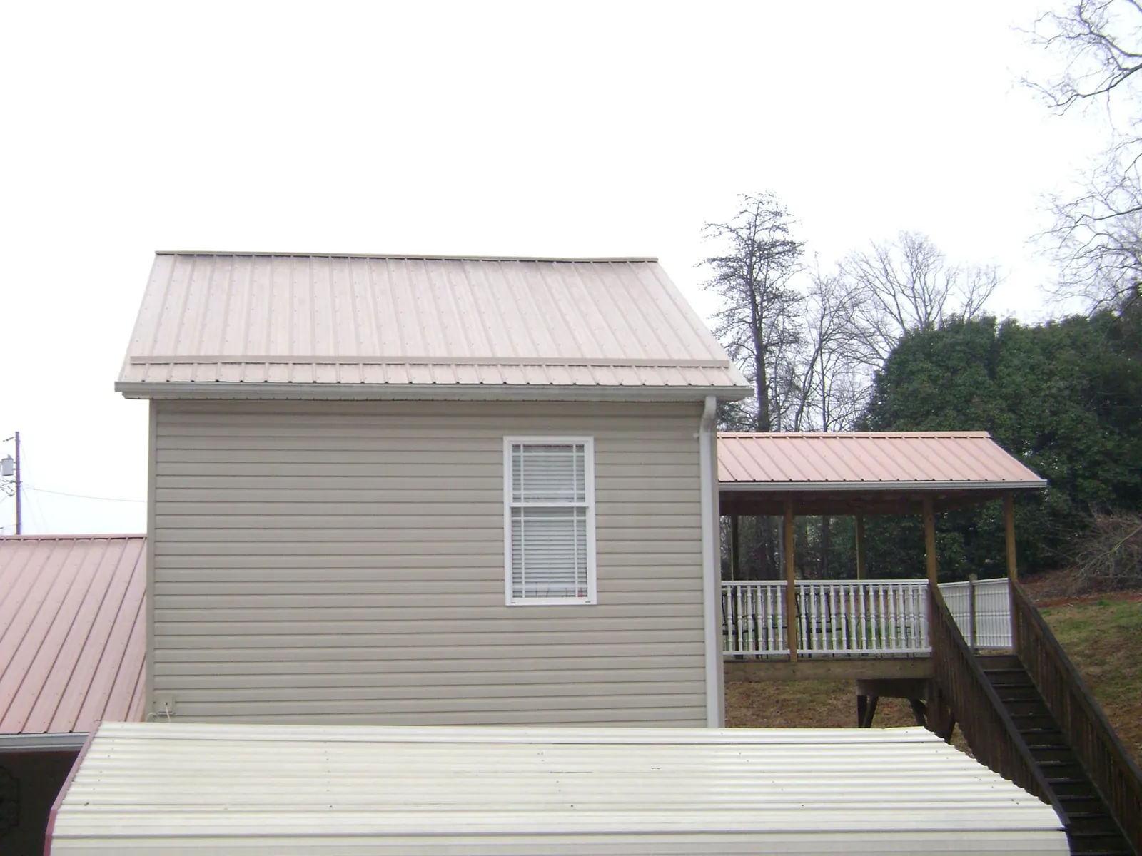 Tan metal roofs on a two story addition and attached porch, from a Roof Replacement job in Glen Dale